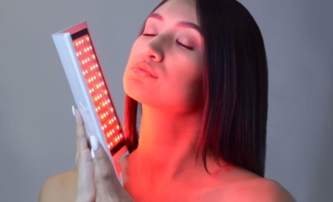 Middle-aged woman holding a red light therapy device to her face.