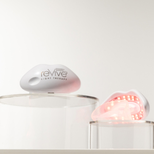 Two Lux Collection Lip Care products with LED lights on sit atop clear acrylic blocks in front of a white background