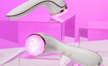 Two Lux Collection Sonique sonic cleansers sit atop clear acrylic blocks; one has a silicone brush head facing the viewer and both have LED lights on