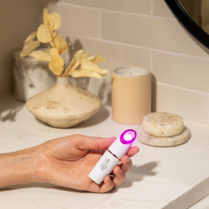 Lux Collection Spot Treatment for Acne in the hand in front of a bathroom countertop with LED lights on.
