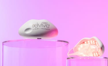 Two LED Technologies reVive Light Therapy Lip Care devices on clear blocks in front of a pink background