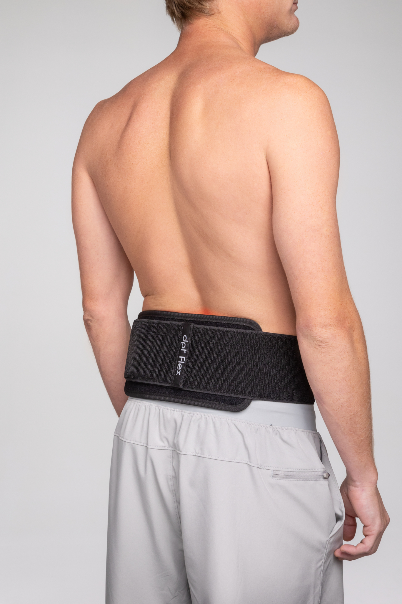 A man is wearing a dpl Flex Pad on his lower back. The device is directly on his skin.