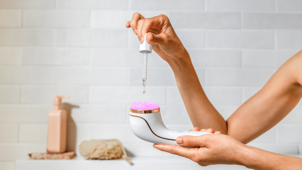 Lux Collection Sonique with serum massage head being held in one hand, while the other hand is using a dropper to apply skincare serum