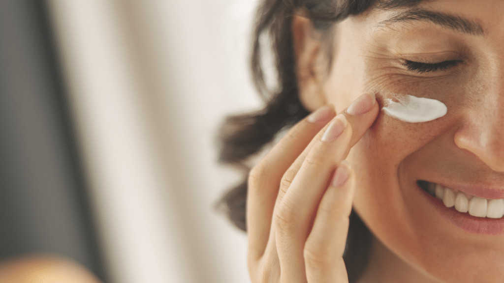 Up-close picture of smiling woman applying moisturizer to her cheek