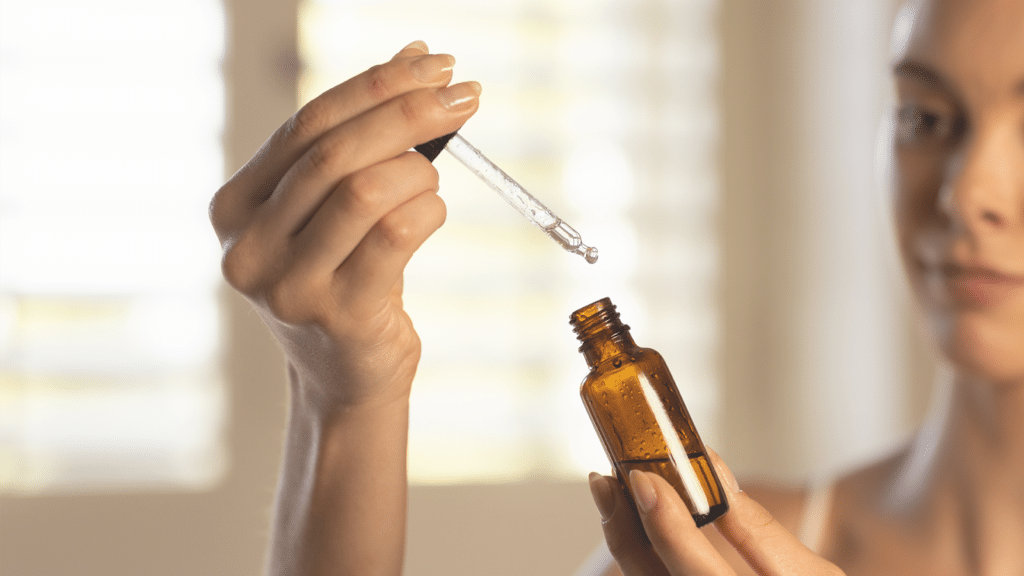 Woman removing dropper filled with skincare serum from an amber bottle